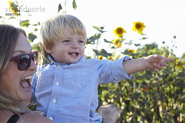 Mittlere erwachsene Frau und Kleinkind-Sohn auf Sonnenblumenfeld zeigend