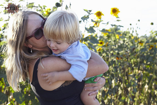 Mittlere erwachsene Frau und Kleinkind umarmend im Sonnenblumenfeld
