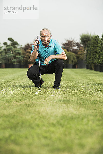 Golfspieler hockt auf dem Rasen und schaut auf den Golfball.