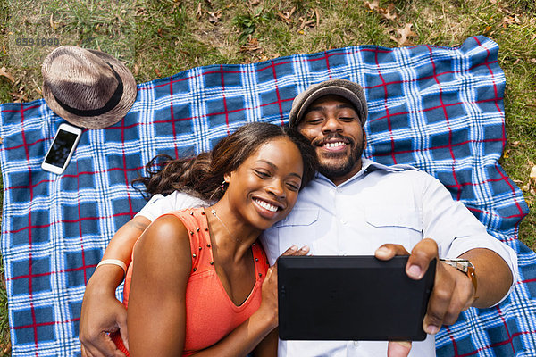 Paar liegt auf Gras und schaut sich den Film auf dem Tablett an.