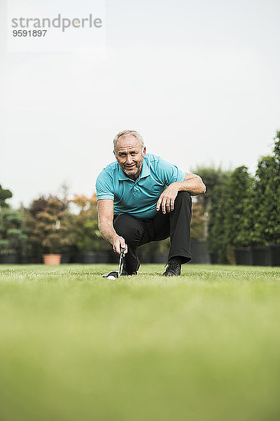 Golfspieler hockt auf dem Rasen und schaut auf den Golfball.