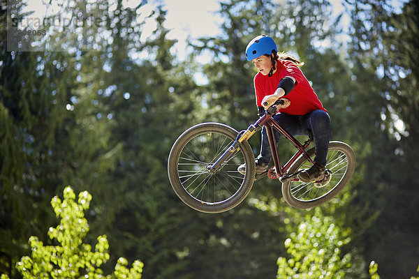 Junge Frau bmx biker jumping mid air im Wald