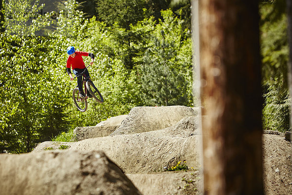 Junge Bikerin  die in der Luft von Felsen im Wald springt.