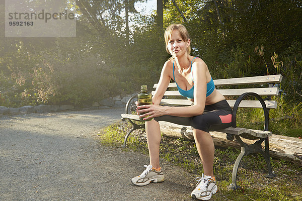 Porträt einer lächelnden Läuferin bei einer Pause auf der Parkbank