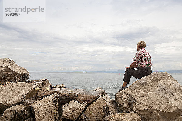 Slowenien  Piran  Frau auf Felsen am Wasser sitzend mit Blick auf den Horizont