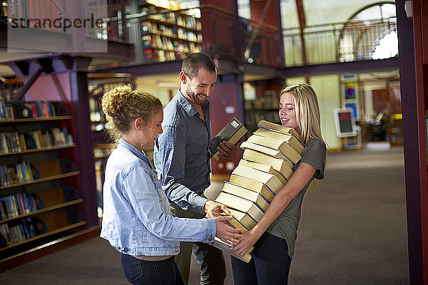 Studentinnen tragen Bücherstapel in einer Bibliothek  die von Freunden unterstützt wird