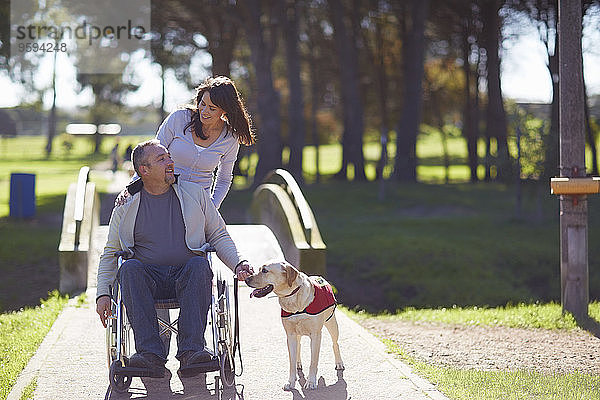 Frau mit Mann im Rollstuhl und Hund im Park
