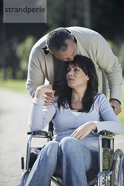 Mann tröstet traurige Frau im Rollstuhl