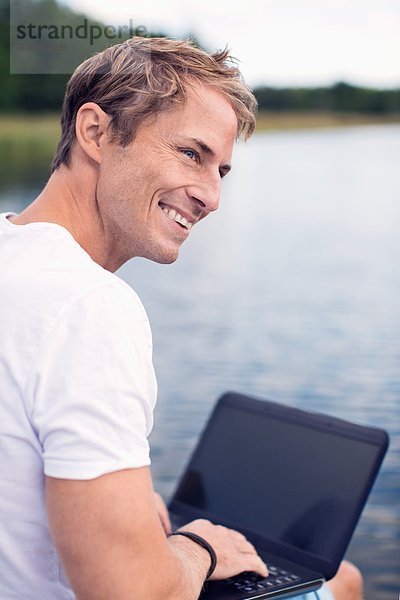 Lächelnder reifer Mann mit Laptop beim Blick auf den See