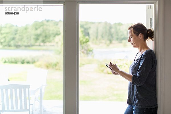 Seitenansicht der Frau mit digitalem Tablett im Stehen am Fenster zu Hause