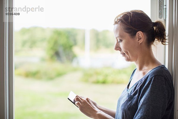 Seitenansicht der Frau mit digitalem Tablett am Fenster zu Hause