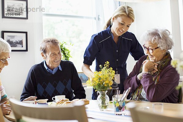 Lächelnde Frau serviert Kaffee für Senioren im Pflegeheim