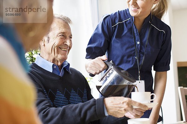Mittelteil einer glücklichen Frau  die dem älteren Mann im Pflegeheim schwarzen Kaffee serviert.