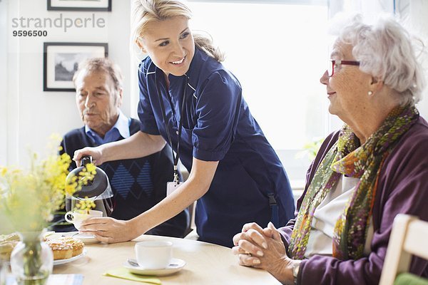 Fröhliche Frau serviert Kaffee für Senioren im Pflegeheim