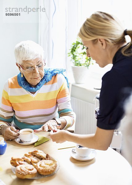 Frau untersucht Finger der Seniorin am Frühstückstisch im Pflegeheim