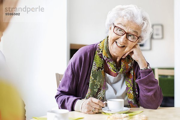 Glückliche Seniorenfrau beim Kaffeetrinken am Frühstückstisch im Pflegeheim