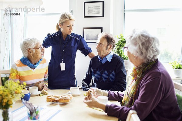 Frau mit Senioren diskutiert am Frühstückstisch im Pflegeheim