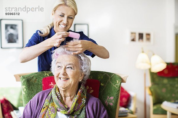 Glückliche Frau  die Lockenwickler an den Haaren der älteren Frau im Pflegeheim anbringt.