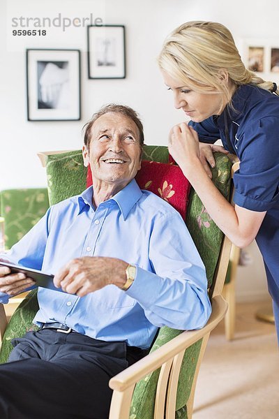 Glücklicher älterer Mann  der weiblich aussieht  während er digitale Tabletten im Pflegeheim benutzt.