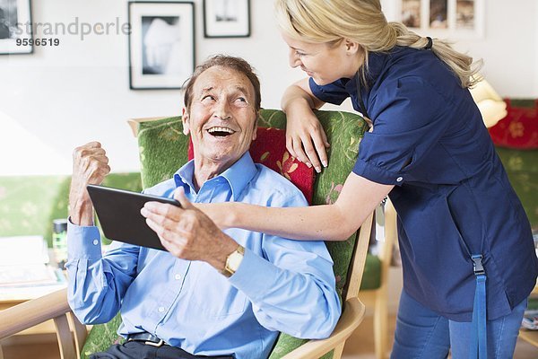Glückliche Senioren und Frauen mit digitalen Tabletts im Pflegeheim