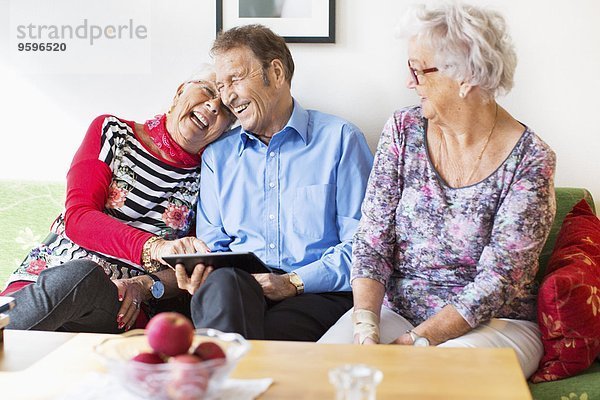 Glückliches Seniorenpaar mit digitalem Tablett von einer Freundin im Pflegeheim