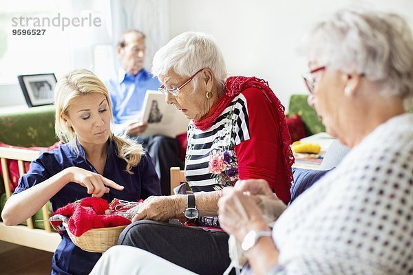 Frau hilft älteren Frauen beim Stricken  während der Mann im Pflegeheim das Buch liest.