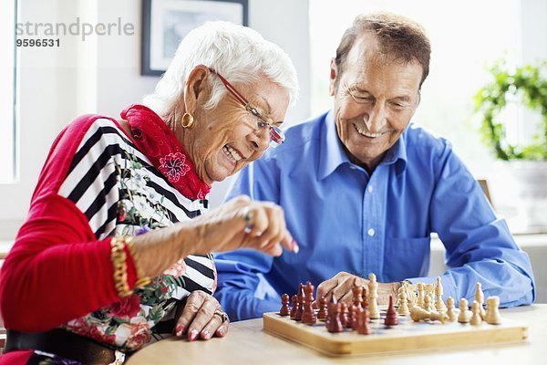 Glückliches Seniorenpaar beim Schachspielen am Tisch im Pflegeheim