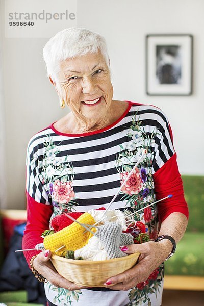 Porträt der glücklichen Seniorin mit Strickkorb im Pflegeheim