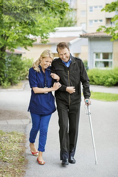 Volle Länge des glücklichen weiblichen Gehens mit behindertem älteren Mann auf der Straße