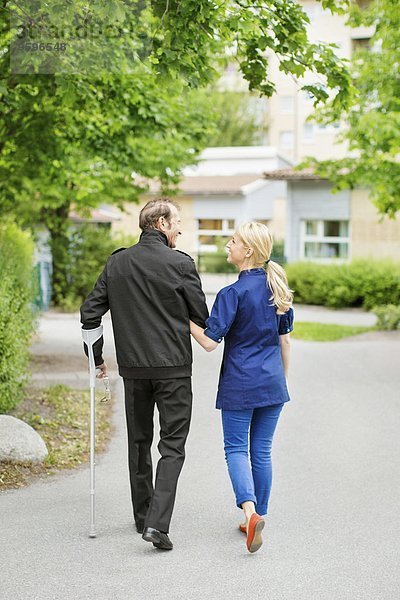 Durchgehende Rückansicht des weiblichen Gehens mit einem behinderten älteren Mann auf der Straße