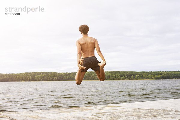 Durchgehende Rückansicht des Mannes  der beim Sprung in den See die Beine hält.