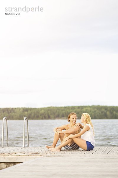 Paar sitzt auf einer Strandpromenade am See gegen den Himmel