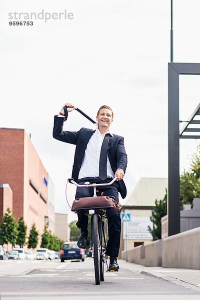 Volle Länge des glücklichen Geschäftsmannes  der beim Radfahren auf der Stadtstraße die Krawatte abnimmt.