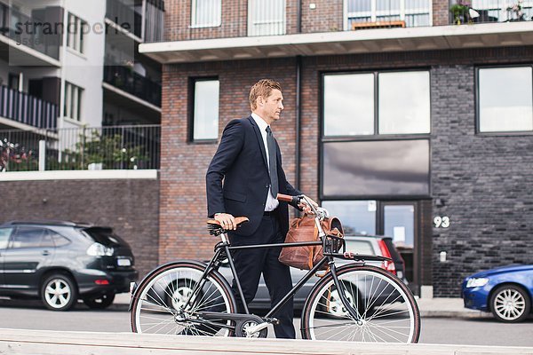 Geschäftsmann  der mit dem Fahrrad auf der Stadtstraße gegen Gebäude läuft
