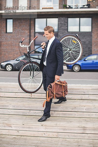 Volle Länge des Geschäftsmannes  der das Fahrrad beim Gehen auf der Treppe trägt