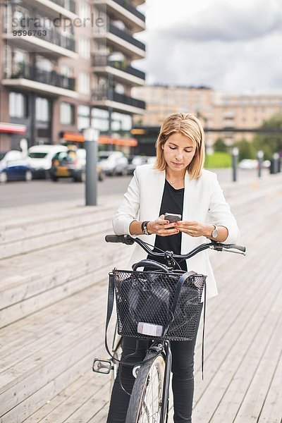 Geschäftsfrau steht mit dem Fahrrad und benutzt das Smartphone in der Stadt.