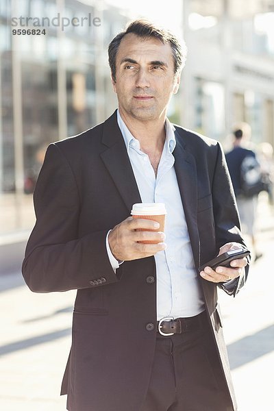 Geschäftsmann schaut weg und hält Handy und Einweg-Kaffeetasse in der Stadt.