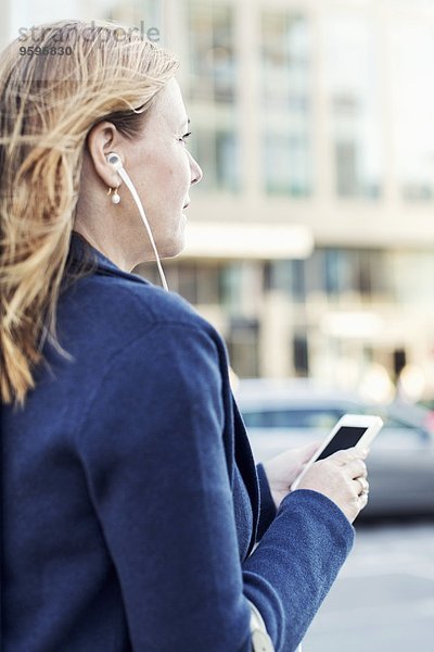 Geschäftsfrau beim Musikhören über Kopfhörer mit dem Handy auf der Straße