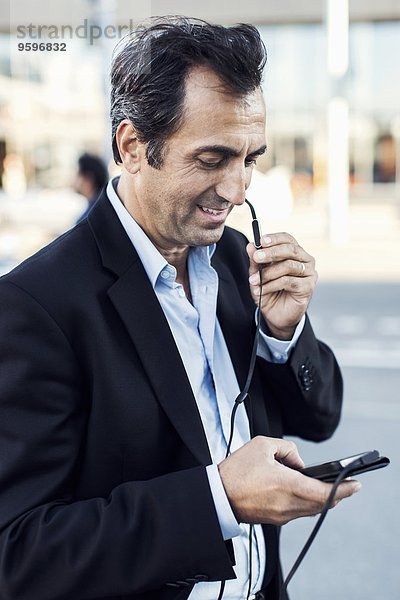 Geschäftsmann  der über Kopfhörer kommuniziert  während er sein Handy auf der Straße benutzt.