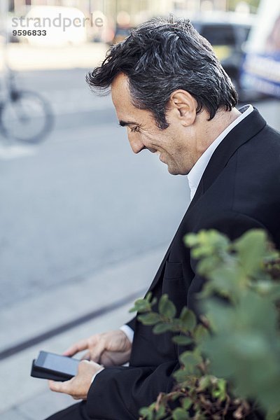 Glücklicher Geschäftsmann mit Handy auf dem Bürgersteig an der Stadtstraße