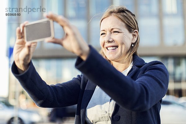 Glückliche Geschäftsfrau beim Fotografieren mit Smartphone im Freien