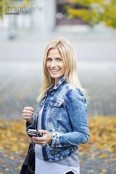 Seitenansicht Porträt einer lächelnden mittleren erwachsenen Frau mit Smartphone im Park