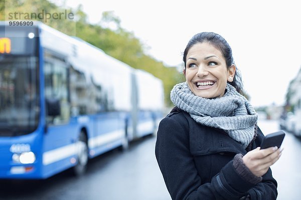 Lächelnde erwachsene Frau  die auf dem Smartphone auf der Straße spricht.