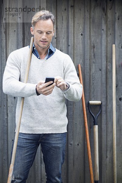 Erwachsener Mann mit Smartphone gegen Holzwand