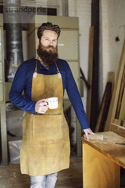 Porträt eines erwachsenen Handwerkers beim Kaffeetrinken in der Orgelwerkstatt