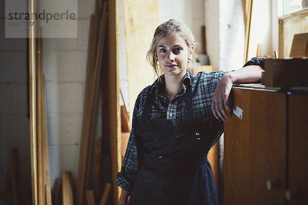 Porträt einer jungen Handwerkerin  die sich auf einen Schrank in der Orgelwerkstatt stützt.