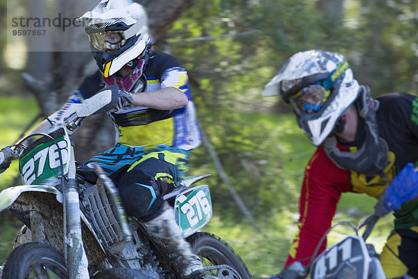 Zwei junge männliche Motocross-Fahrer rasen durch den Wald