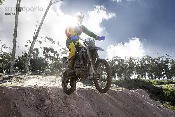 Junger männlicher Motocross-Rennfahrer springt in der Luft den Schlammberg hinunter