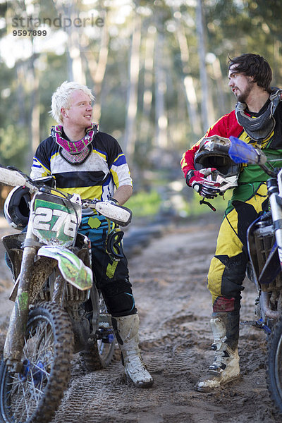 Zwei junge männliche Motocross-Fahrer im Gespräch auf der Waldstrecke