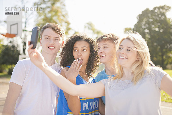 Vier junge erwachsene Basketballspieler mit Smartphone Selfie auf dem Platz